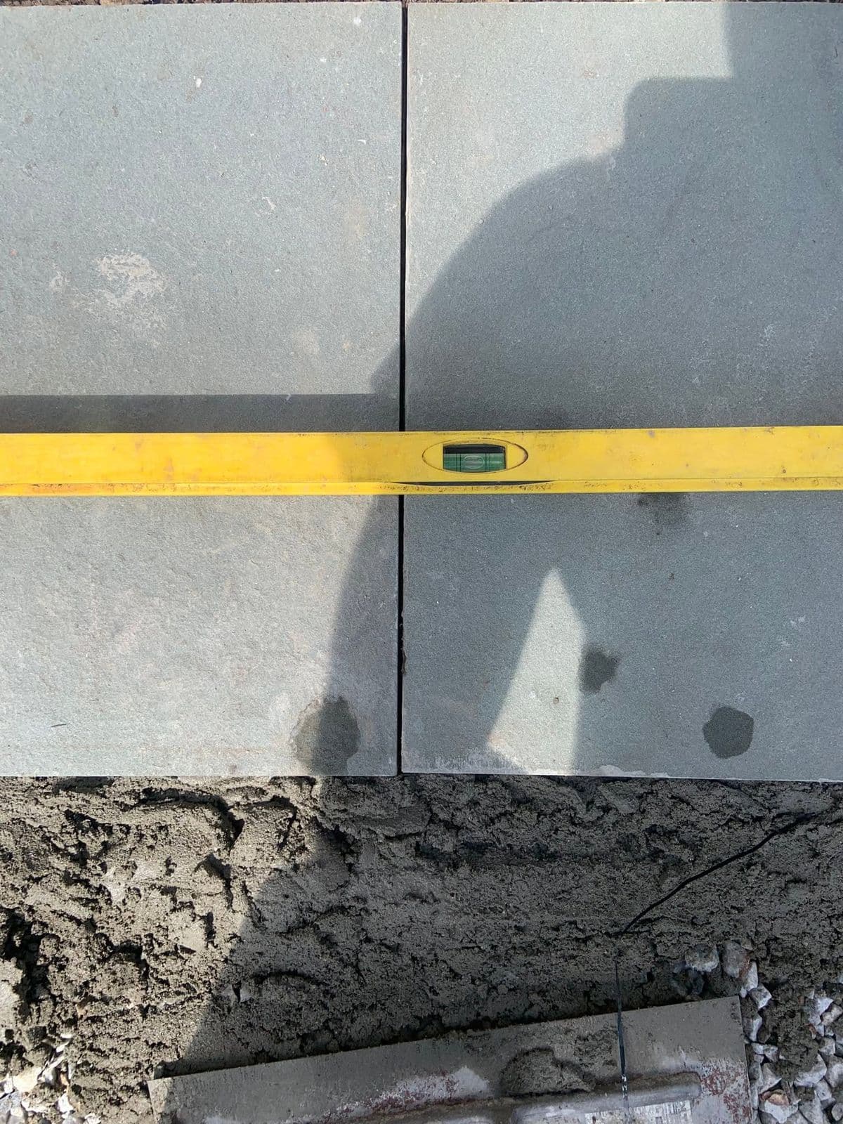 Close-up of a yellow level checking two gray stone pavers set in wet mortar