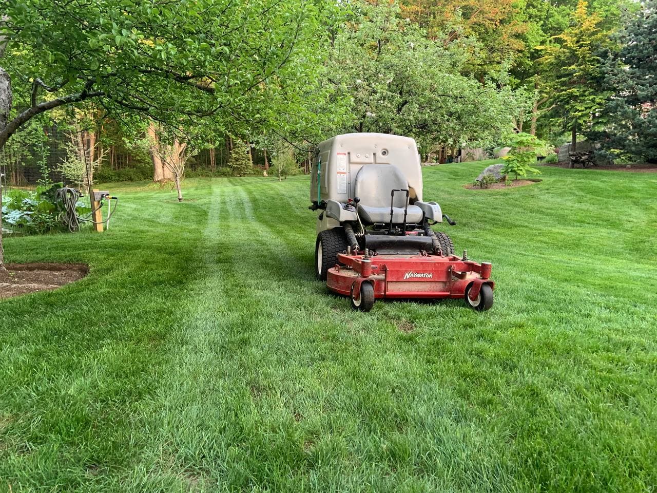 Exmark zero-turn mower parked on a freshly striped lawn under leafy fruit trees at dusk