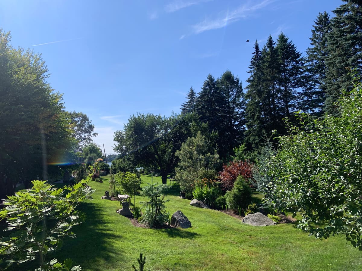 A Bellamy-maintained Seacoast waterfront property with layered garden beds, boulders, and a lawn sloping toward the water